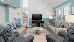 A spacious living room with a ceiling fan, a large flat-screen TV, and two sofas with patterned cushions. - A Pier to Sea: Elegant Home with Private Pool, Hot Tub, Expansive Deck (Oak Island)