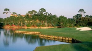 Un parcours de golf avec des obstacles d’eau, des bunkers de sable et une zone boisée en arrière-plan.