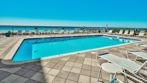 Une piscine rectangulaire, bordée d’une terrasse carrelée, entourée de chaises longues blanches et d’une clôture en métal.
