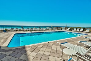 Una piscina rectangular con solárium empedrado, rodeada de sillones blancos y una cerca metálica.