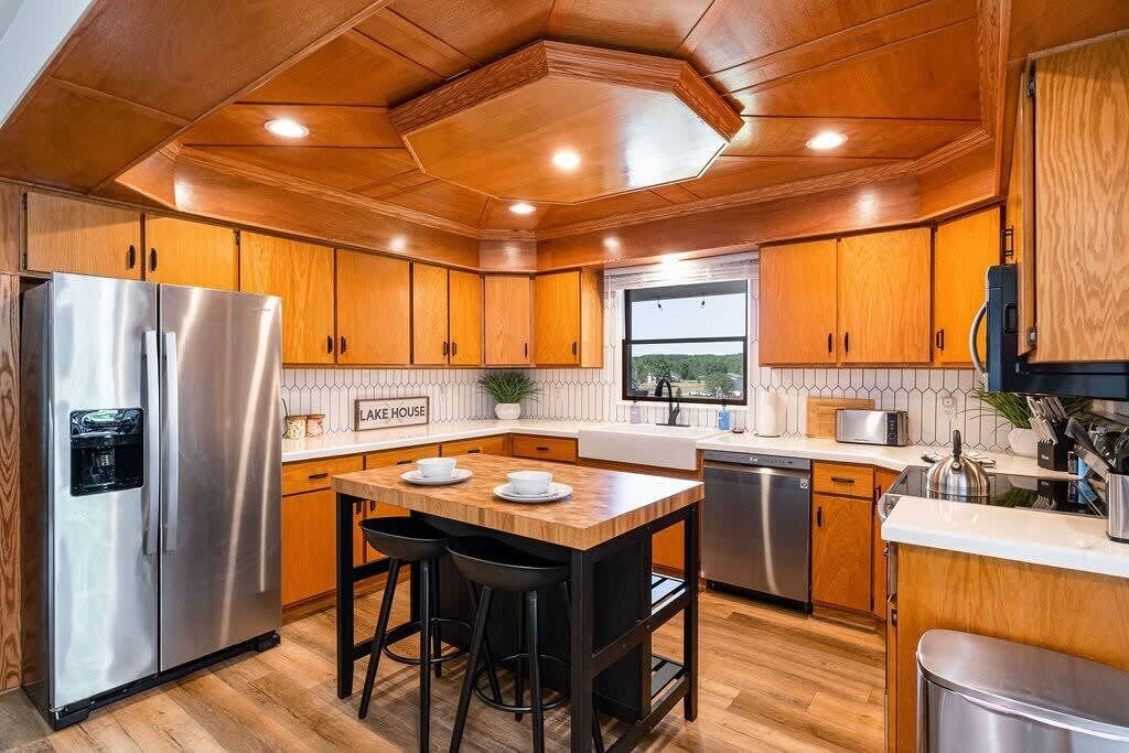 Une cuisine moderne avec des meubles en bois, des appareils électroménagers en acier inoxydable et un îlot central doté de tabourets.