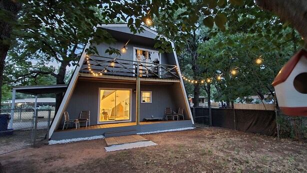 A modern, two-story house with a large glass door and windows, surrounded by trees and a fence. - Private A-Frame w/Kayaks on Canal newly renovated (Granbury)