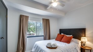 A neatly made bed with white linens and two rolled towels, a bedside table with a lamp, and a window with curtains. - Private A-Frame w/Kayaks on Canal newly renovated (Granbury)