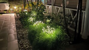 Ett utomhusområde som är avsett för användning på kvällen, med en asfalterad gångväg, dekorativ belysning och en stor blomlåda.