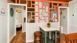 A room with a wooden ceiling, a white door, a bed, a table with two stools, and a wall with a grid pattern and an anchor decoration. - Saltwater Pool, Large Dog Friendly, Steps to the beach!  (North Myrtle Beach)