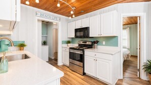A kitchen with white cabinets, a black microwave, a stainless steel stove, and a sign that reads 'BEACH LIFE'. - Saltwater Pool, Large Dog Friendly, Steps to the beach!  (North Myrtle Beach)