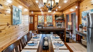 A wooden interior with a dining table set for six, a kitchen area, and a large window. - Pool! Hot Tub - Movie Room - Game Room - Dollywood (Sevierville)