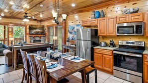 A wooden cabin kitchen with a dining area, stainless steel appliances, and a large window overlooking greenery. - Pool! Hot Tub - Movie Room - Game Room - Dollywood (Sevierville)