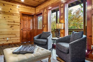 A cozy cabin interior with wooden walls, two grey armchairs, a white cushioned bench, and a wooden door. - Pool! Hot Tub - Movie Room - Game Room - Dollywood (Sevierville)