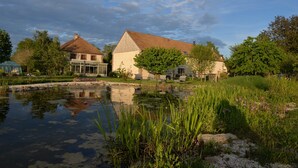 A serene pond with surrounding greenery and two buildings with pitched roofs. - LA MELINOTHE (Paisy-Cosdon)