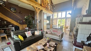 A spacious living area with a high ceiling, a staircase, a dining area, and a kitchen. - LA MELINOTHE (Paisy-Cosdon)