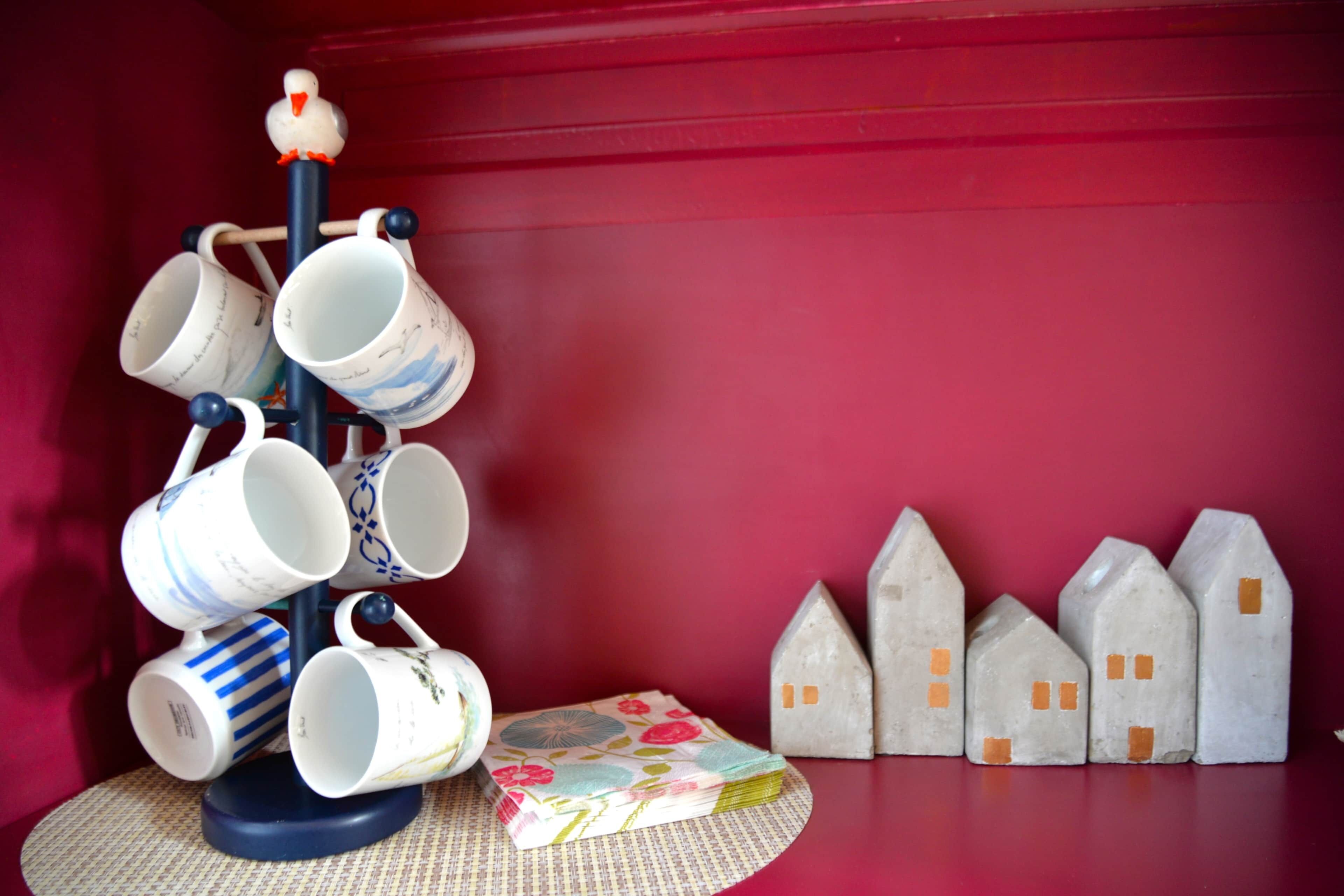 A collection of ceramic mugs on a stand, a small house-shaped object, and a patterned mat.