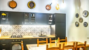 Une cuisine avec des meubles de couleur sombre, un pare-feu en carreaux et un coin repas avec des chaises et une table en bois.