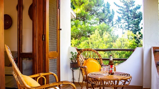 Un balcon agrémenté de meubles en osier, une table avec des bouteilles et une vue sur la verdure.