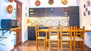 Une cuisine de taille réduite, avec des meubles de couleur sombre, un pare-feu en carreaux et une table à manger en bois, assortie de chaises.