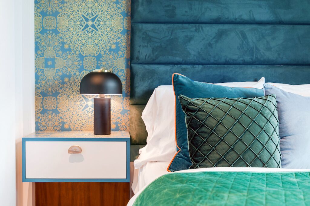 Een opgemaakt bed met een groene sprei, een blauw hoofdeinde en een behang met patroon.