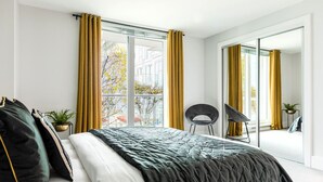A modern bedroom with a large bed, a chair, and a view of the outdoors through a sliding glass door. - HUGE THAMES VIEW LUXXE NOMAD DESIGN HOME (London)