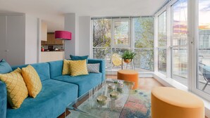 A modern living room with a blue sofa, a glass coffee table, and a large window offering a view of the city. - HUGE THAMES VIEW LUXXE NOMAD DESIGN HOME (London)