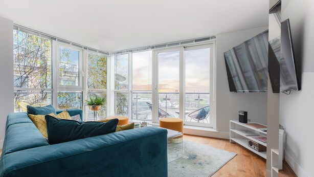 A modern living room with a teal sofa, large windows, a flat-screen TV, and a view of the city. - HUGE THAMES VIEW LUXXE NOMAD DESIGN HOME (London)