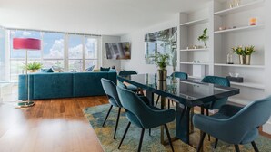 A modern living room with a glass dining table, teal sofas, and a large window with a city view. - HUGE THAMES VIEW LUXXE NOMAD DESIGN HOME (London)