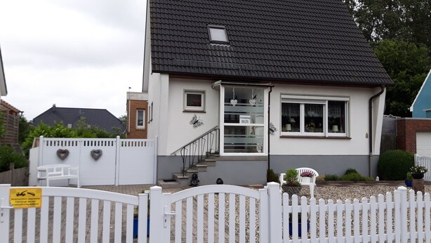 Une maison à deux étages, avec une façade blanche, un toit noir et une clôture blanche faite de piquets.