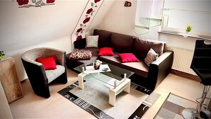 Un salon avec un canapé marron, un fauteuil en osier et une table basse en verre.
