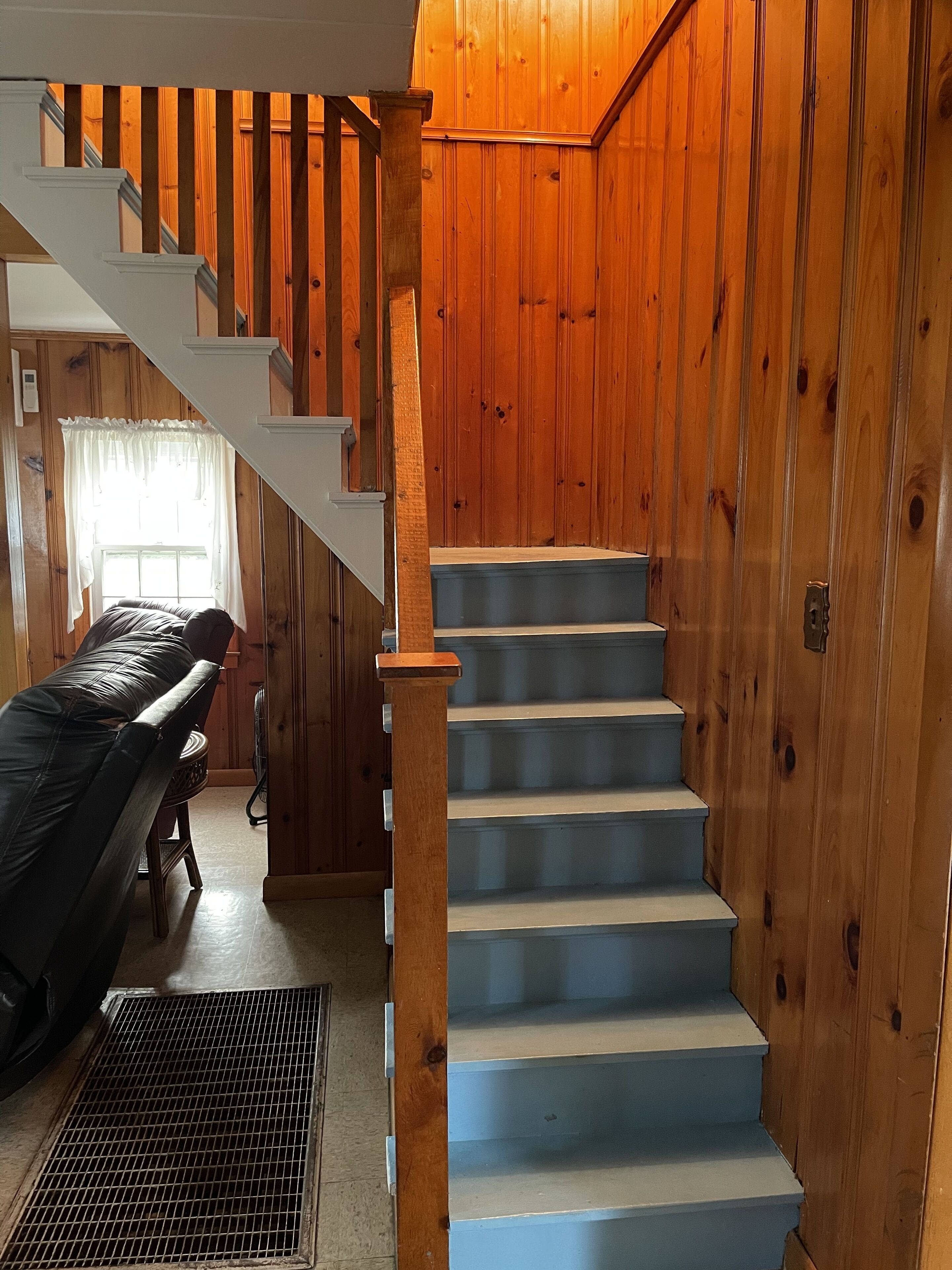 A wooden interior with a staircase, a leather chair, and a window with curtains.