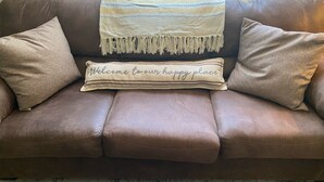 A brown leather sofa with a beige throw blanket and a pillow with "Welcome to our happy place" text. - Remodeled Home - Near Faurot Field! (Columbia)