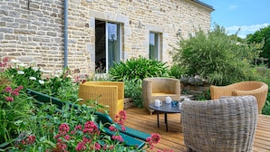 A stone building with a wooden deck, wicker furniture, and a variety of plants. - Ker Case A Nou - Longère à la campagne (Monterblanc)