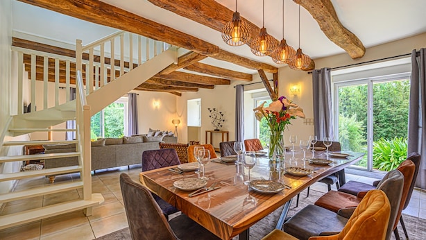 A dining area with a wooden table, cushioned chairs, and a staircase leading to an upper level. - Ker Case A Nou - Longère à la campagne (Monterblanc)