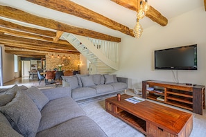 Uma sala de estar moderna com vigas de madeira aparentes, um sofá seccional cinza, uma mesa de centro de madeira e uma TV de tela plana.
