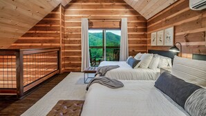 Ein Schlafzimmer einer Holzhütte mit zwei Betten, einer Sitzbank und Blick auf einen bewaldeten Berg.