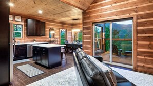 Ein Blockhaus-Interieur mit Küche, Essbereich und einer großen Glaswand zu einer Terrasse.
