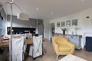 Une cuisine moderne avec des meubles de couleur grise, une table à manger en bois et un fauteuil jaune.