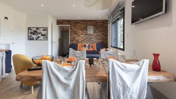 A modern dining area with a wooden table set for four, white chairs, and a large pendant light. - Le Château D'Ancelle (Ancelle)