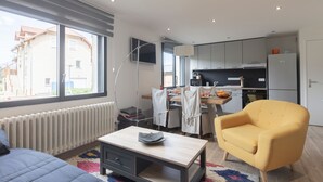 A modern apartment with a large window, a kitchen area, a yellow armchair, and a small table. - Le Château D'Ancelle (Ancelle)