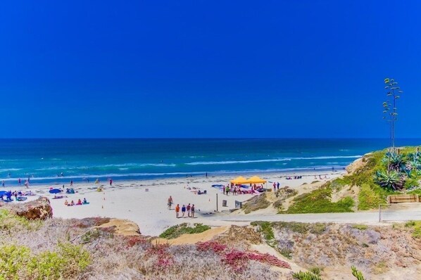 A beach with people, a yellow tent, and a rocky outcrop.