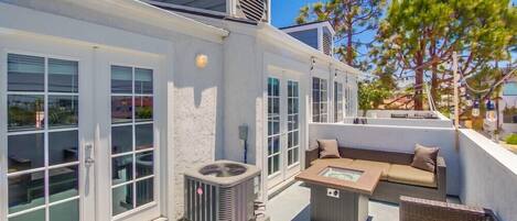 A rooftop patio with outdoor furniture, a glass door entrance, and an air conditioning unit.
