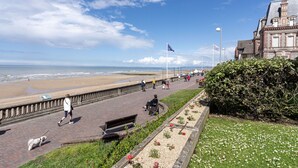 Eine Uferpromenade mit gepflastertem Gehweg, Bänken und einer Rasenfläche mit Blumen.