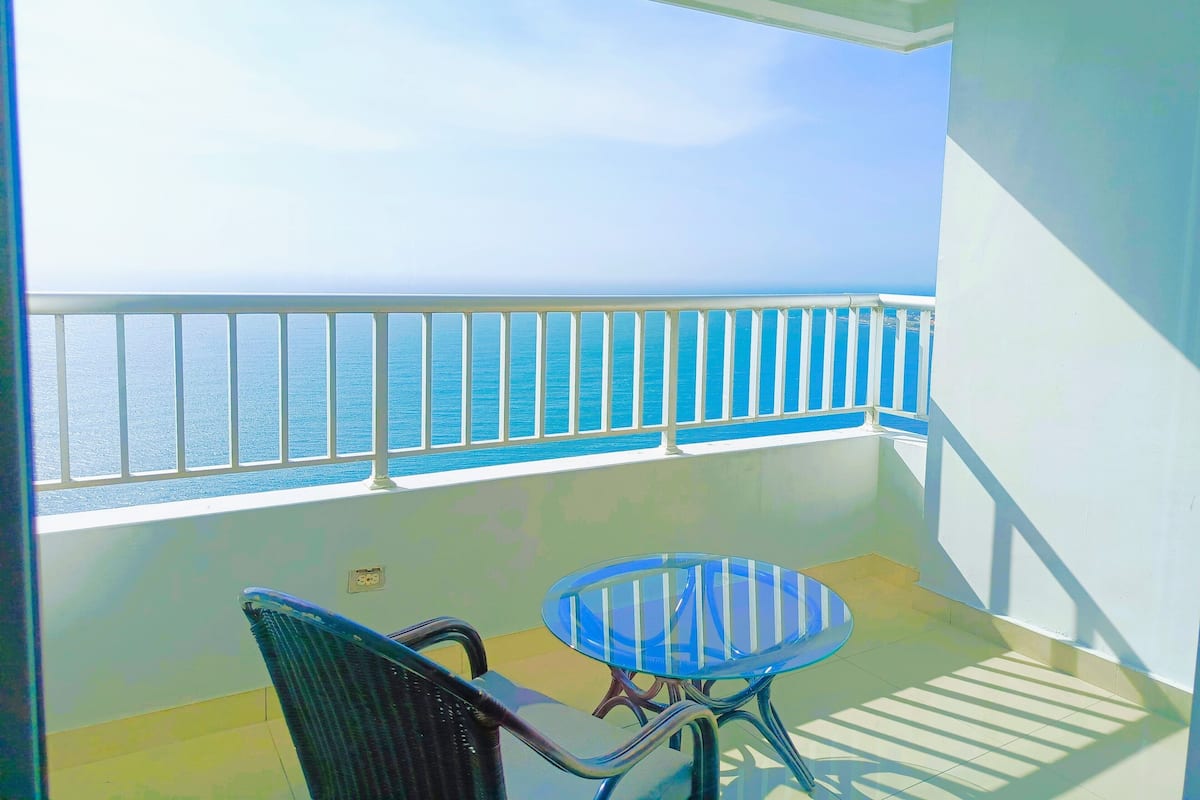 Un balcon avec vue sur la mer, une balustrade blanche et une petite table avec des chaises.