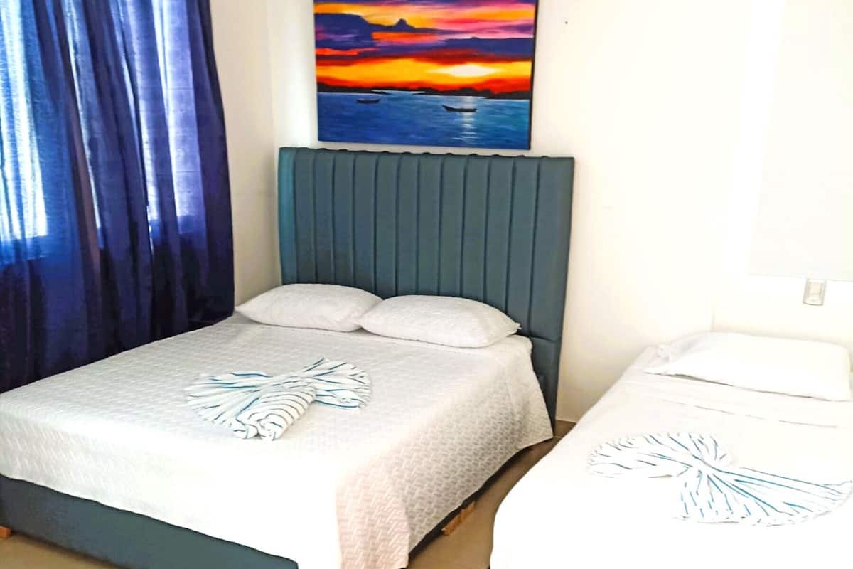 Une chambre à coucher avec un lit, une tête de lit, un tableau et un rideau.