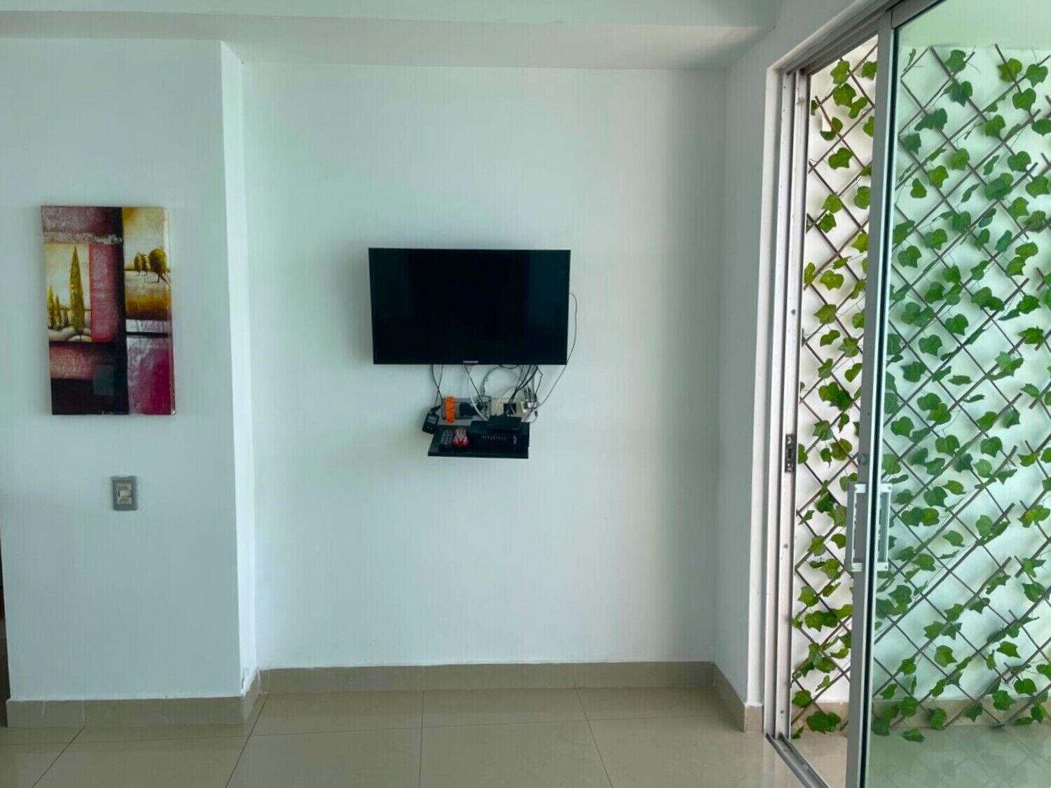 Una stanza con una TV a schermo piatto montata a parete, una ciabatta multipresa sottostante e una porta in vetro decorata con un motivo a foglia verde.