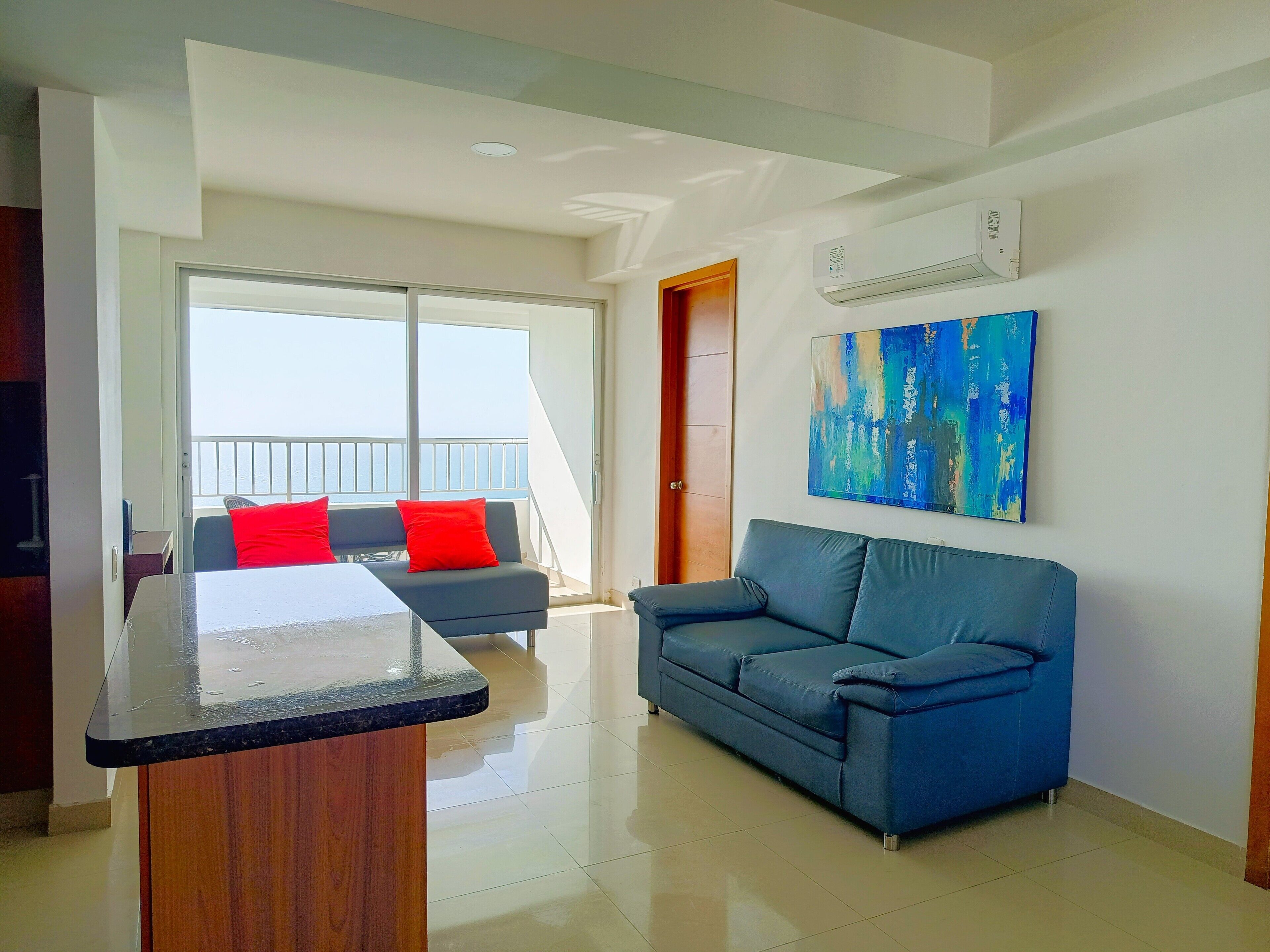 Ein modernes Wohnzimmer mit einem blauen Sofa, einem Holztisch und einem großen Fenster mit Blick auf das Meer.