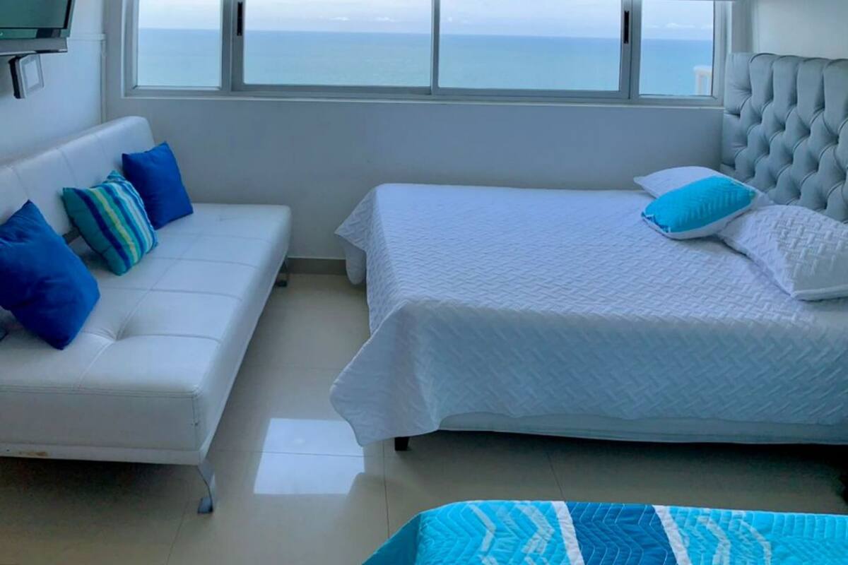 Une chambre à coucher avec un lit, un canapé, une télévision et une fenêtre donnant sur la mer.