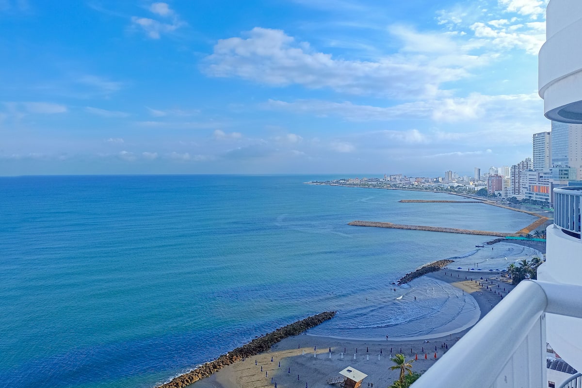 Un paysage urbain côtier offrant une vue dégagée sur l’océan et une plage parsemée de parasols et de personnes.