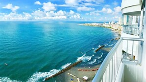 A coastal view from a balcony with a clear sky, ocean, and a distant cityscape. - Apartamentos | Frente al Mar + Primera Linea de Playa | Piscina TOP (Cartagena)