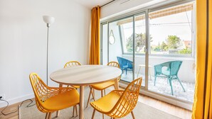 Een moderne kamer met een ronde tafel en gele stoelen, grote ramen met gele gordijnen en uitzicht naar buiten.