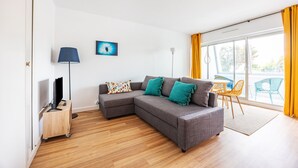 Een moderne woonkamer met een grijze modulaire bank, een klein houten bijzettafeltje met een televisie, een vloerlamp en een kleurrijk schilderij aan de muur.