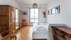 Une chambre à coucher comprenant un lit, une armoire en bois, une chaise pliante rouge, un bureau et une fenêtre donnant sur un paysage agréable.