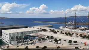 Un port de plaisance où est amarré un grand voilier, un bâtiment moderne portant l’inscription « COSQUER MEDiterranee », et une vue dégagée sur la mer et le paysage lointain.